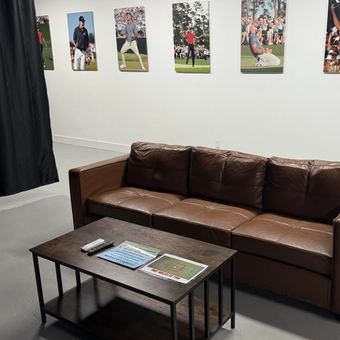 A leather sofa and coffee table at FlagShots in Dunedin, FL, beneath framed prints of major championship moments