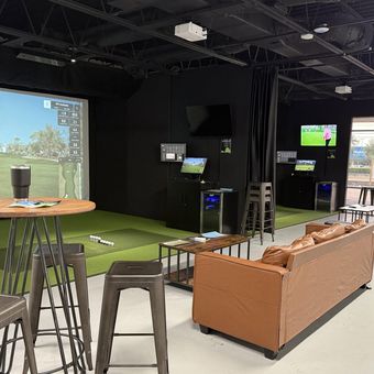 Bar-height tables and stools set between the two simulator bays at FlagShots in Dunedin, FL