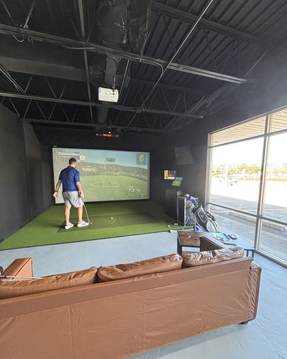 A golfer mid-swing in a FlagShots golf simulator bay in Dunedin, FL, hitting into the impact screen